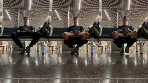 Un mec filmé assis jambes écartées sur un banc public