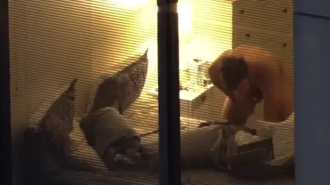 Un twink nu se penche dans une chambre baignée de lumière